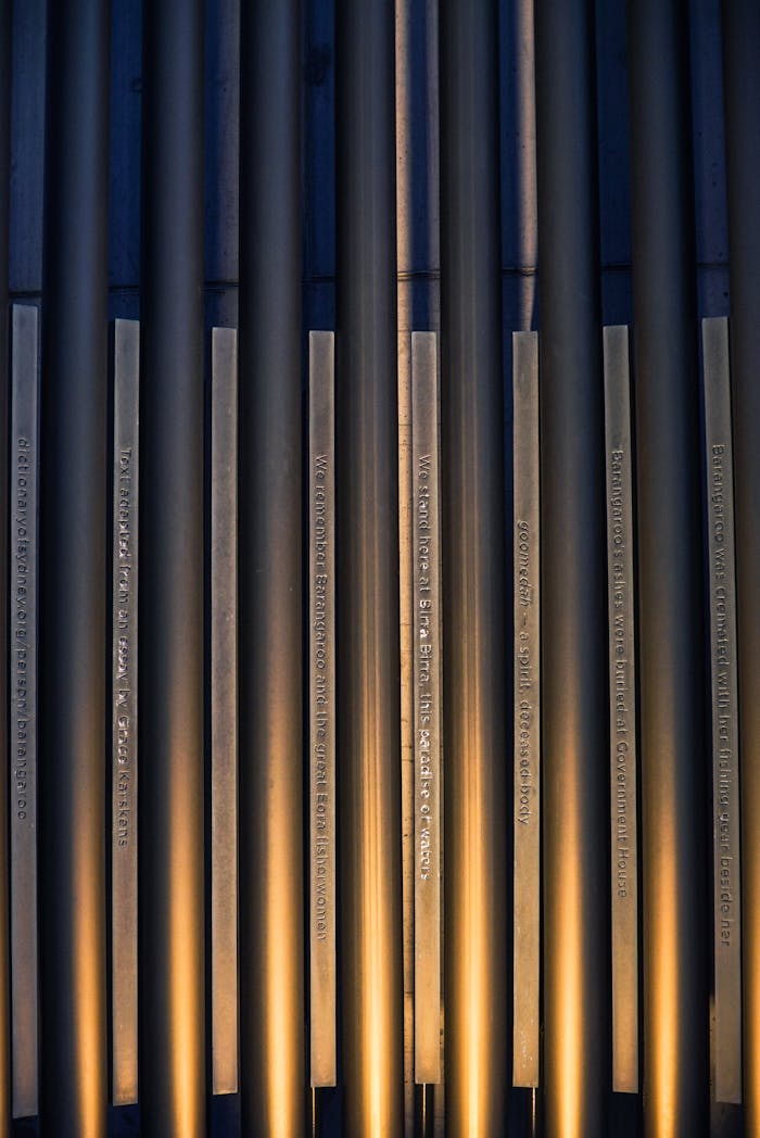 team-04 A sophisticated abstract photograph showcasing vertical metal pipes illuminated by golden lighting.