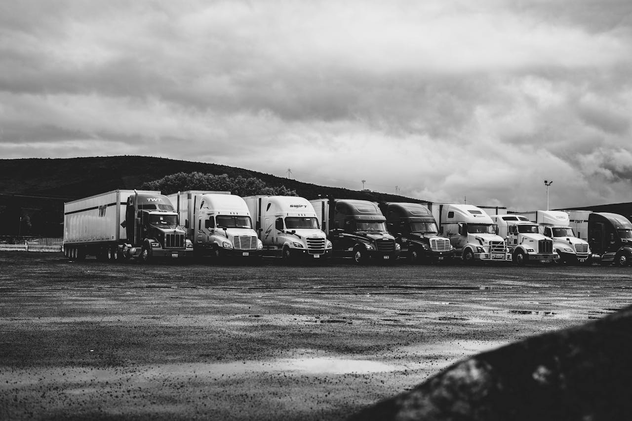 team-01 Row of parked semi trucks in a rainy lot, captured in a dramatic black and white setting.